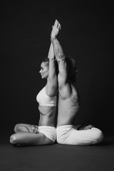 Monochrome portrait of beautiful sporty couple: woman and man in white clothes doing yoga asanas together indoor 