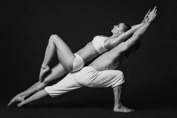 Monochrome portrait of beautiful sporty couple: woman and man in white clothes doing yoga asanas together indoor 