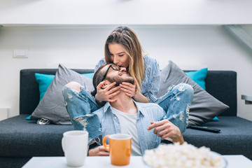 Wall Mural - Young couple sitting on the couch, drinking coffee and watching tv