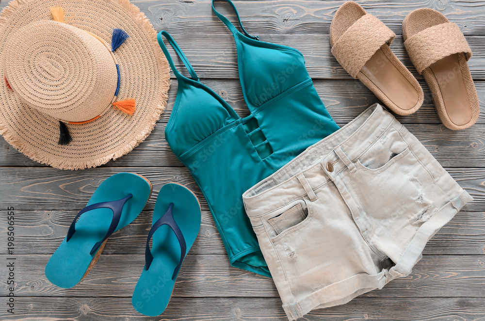 Womens clothing, accessories (denim shorts, straw hat, swimsuit, sandals) on grey wooden background. Trendy fashion outfit. Shopping, travel, summer, beach concept, abstract.  Flat lay - obrazy, fototapety, plakaty 