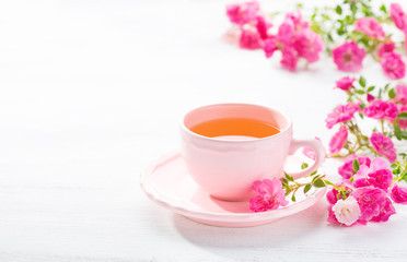 Cup of tea and branch of small pink  roses on  white rustic table.