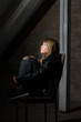 trauriges Teenager Mädchen auf einem Stuhl im Dunkeln sitzend und zum Fenster guckend