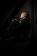 trauriges Teenager Mädchen auf einem Stuhl im Dunkeln sitzend und zum Fenster guckend