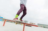 Fototapeta Na sufit - A close-up of a teenager's leg of a skateboarder glides on a skateboard along the railing in the skatepark. The concept of moving forward at a young age. Teenage Sports