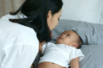 young beautiful asian mother caring and playing with her baby in the bedroom on a bright morning sun