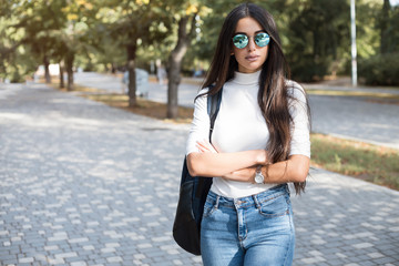 Wall Mural - Hipster girl wearing khaki white sweat,t-shirt, jeans and back pack posing walking in autumn city, minimalist urban clothing style.Stylish happy young woman wearing boyfriend jeans and blue sunglasses