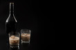 Coffee liqueur and alcoholic beverages based on milk and whiskey concept with Irish cream bottle and glasses with ice isolated on dark black background with copy space