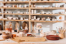 Brushes, Paints And Wooden Shelves With Ceramics In Pottery Workshop