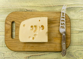 Cheese on cutting board  and knife on wooden background