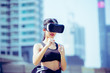 A young beautiful girl in virtual reality glasses makes sport and aerobics in the city. Future technology concept.