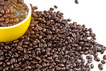 Closeup group of roasted coffee beans on white background,beside blurred yellow ceramic cup,warm light tone,blurry light around.