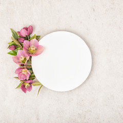 Creative layout with purple colorful flowers, green leaves and circle paper note card on stone beige background. Flat lay, top view and copy space. Minimal nature concept