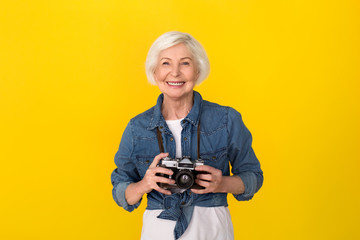 Senior woman traveler studio isolated on yellow wall holding camera cheerful