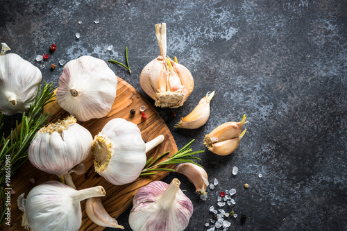 Fotografía Garlic cloves with spices and herbs on a dark stone background.