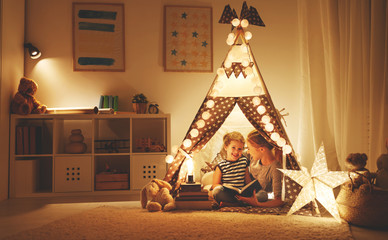 mother and child daughter reading a book and a flashlight before going to bed