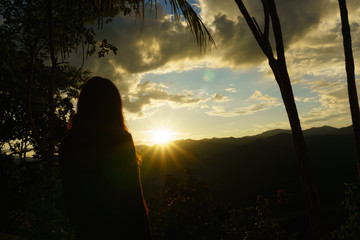 Wall Mural - silhouette of asian female with amazing wild nature view of layer of mountain forest landscape with cloudy sky when sunset or twilight. Natural green scenery of cloud and mountain slopes background.