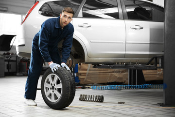 Poster - Young mechanic with car tire in service center