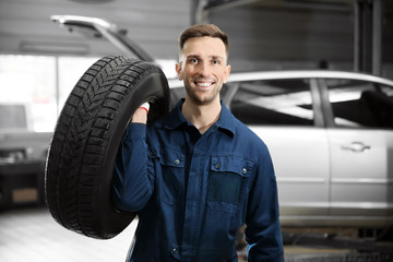 Poster - Young mechanic with car tire in service center