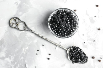 Spoon and bowl with delicious black caviar on grey background