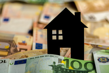 A black paper house with euro banknotes in background