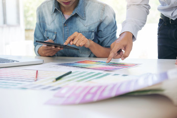 Poster - Two young interior design or graphic designer working on project of architecture drawing with work tools and color swatches, colour chart in digital tablet at workplace