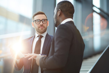 Wall Mural - Confident delegate with tablet looking at his business partner while making presentation of his speech points for conference