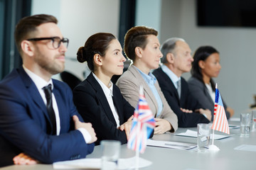 Group of international representatives in formalwear listening attentively report of one of speakers at political summit