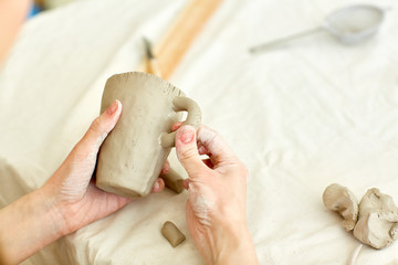 Human hands putting handle on clay mug while finishing work over this item