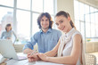 © pressmaster - Portrait of smiling pretty businesswoman sitting at the table with her colleagues in the background