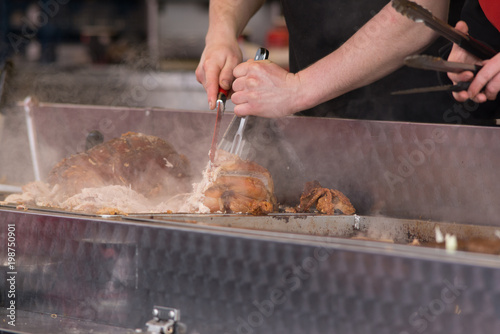 Fotografía man carving pork joint with fork and knife at hog roast