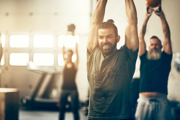 Wall Mural - Smiling young man swinging weights during a gym exercise class