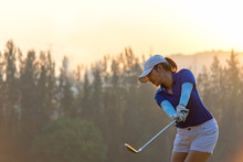 Asian Woman Golf Player Doing Golf Swing Tee Off On The Green Sunset Evening Time, She Presumably Does Exercise. Healthy And Lifestyle Concept.