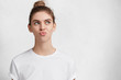 © WHstudio Leushin N - Portrait of discontent pensive female with blue eyes pouts lips and looks thoughtfully upwards, dressed in casual t shirt, isolated over white background. People, emotions, facial expressions concept