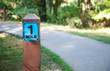 A one mile marker sign post beside a paved pathway with a bright green and sunny background.
