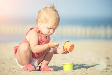 Baby playing on the sandy beach near the sea. Cute little girl in red dress with sand on tropical beach. Ocean coast.