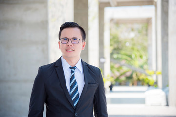 Wall Mural - Young asian businessman wearing suit and smile on modern buiding background