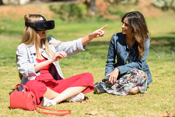 Two women looking in VR glasses and gesturing with his hands outdoor