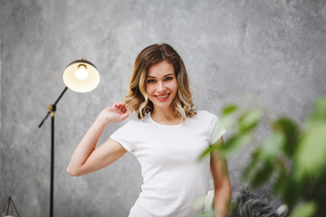 Portrait of a young beautiful woman on a gray background. A cute girl in a white T-shirt looks at the camera and smiles, close-up.