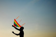 © ruslanshug - silhouette of active young man operating multicolor kite flying in air at summer sunset with copyspace