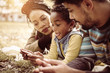 © Mladen - African American parents in park with daughter using mobile phone together.