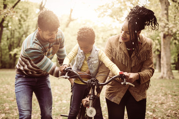 Canvas Print - Smiling African American parents teaching their little girl to driving bike in park.