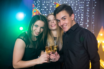 Three young men and two women in hoods and with glass champagne celebrate a birthday have fun in a nightclub