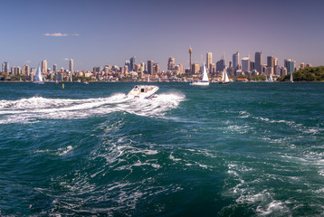 A speedboat heads towards the sky line of downtown Sydney and yatchs sailing within Sydney harbour, Australia