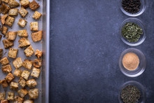 Flay lay of croutons on a baking sheet, opposite a row of spices, and space for text in the middle