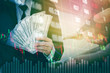© joyfotoliakid - Businessman Holding money US dollar bills on digital stock market financial exchange information and Trading graph background