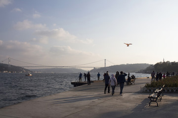 People walk by Bosphorus strait in Istanbul. FSM bridge is in the background.