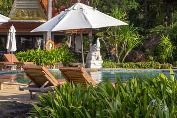 Beautiful beach with swimming pool, palm trees, daybeds and umbrella in a tropical garden near sea