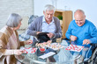 © Seventyfour - Portrait of senior people playing lotto game sitting at glass table in living room of retirement home