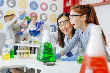 wonders of chemistry. charming chemistry teacher pouring blue chemical into a green one and smiling 