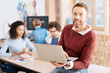 © Viacheslav Yakobchuk - Great day. Handsome exuberant bearded man holding his laptop and sitting on the table while his colleagues working in the background